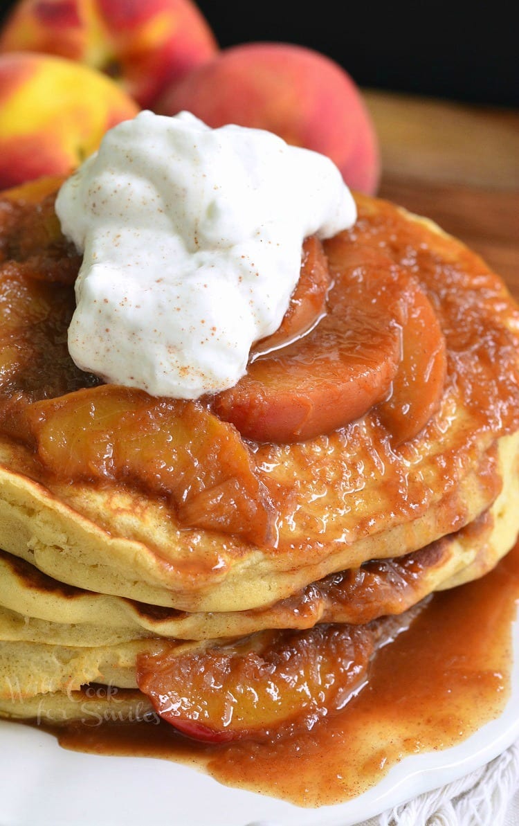 Buttermilk Pancakes with peaches on and whip cream on top and homemade syrup on a white plate 