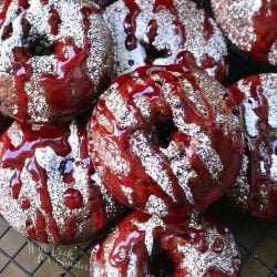 Raspberry chocolate doughnuts on a wire cooling rack topped with powdered sugar and raspberry glaze as viewed from above