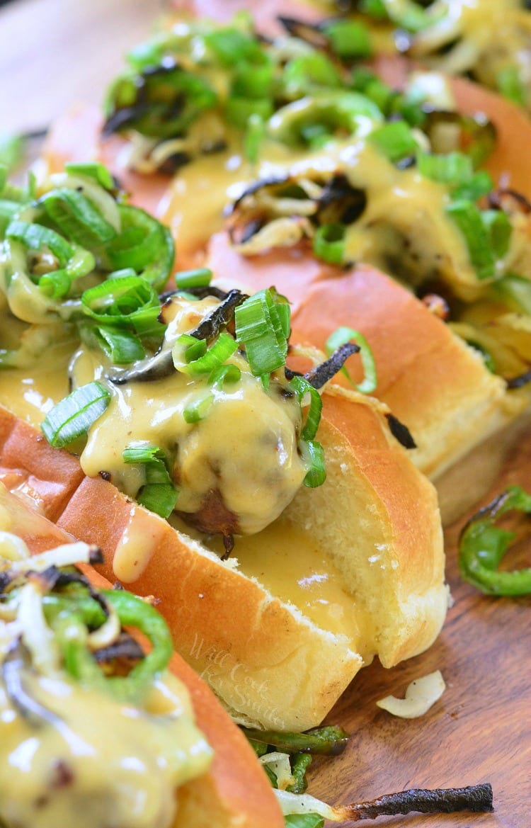 Brats in a bun with cheese sauce onions, green peppers, and green onions on top 