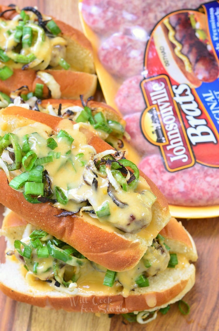 Brats in a bun with cheese sauce onions, green peppers, and green onions on top and pack of johnsville brats to the right 