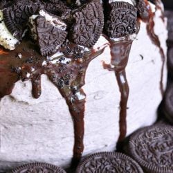 Chocolate orea cake on a wooden table with additional oreo cookie around the bottom of the cake.