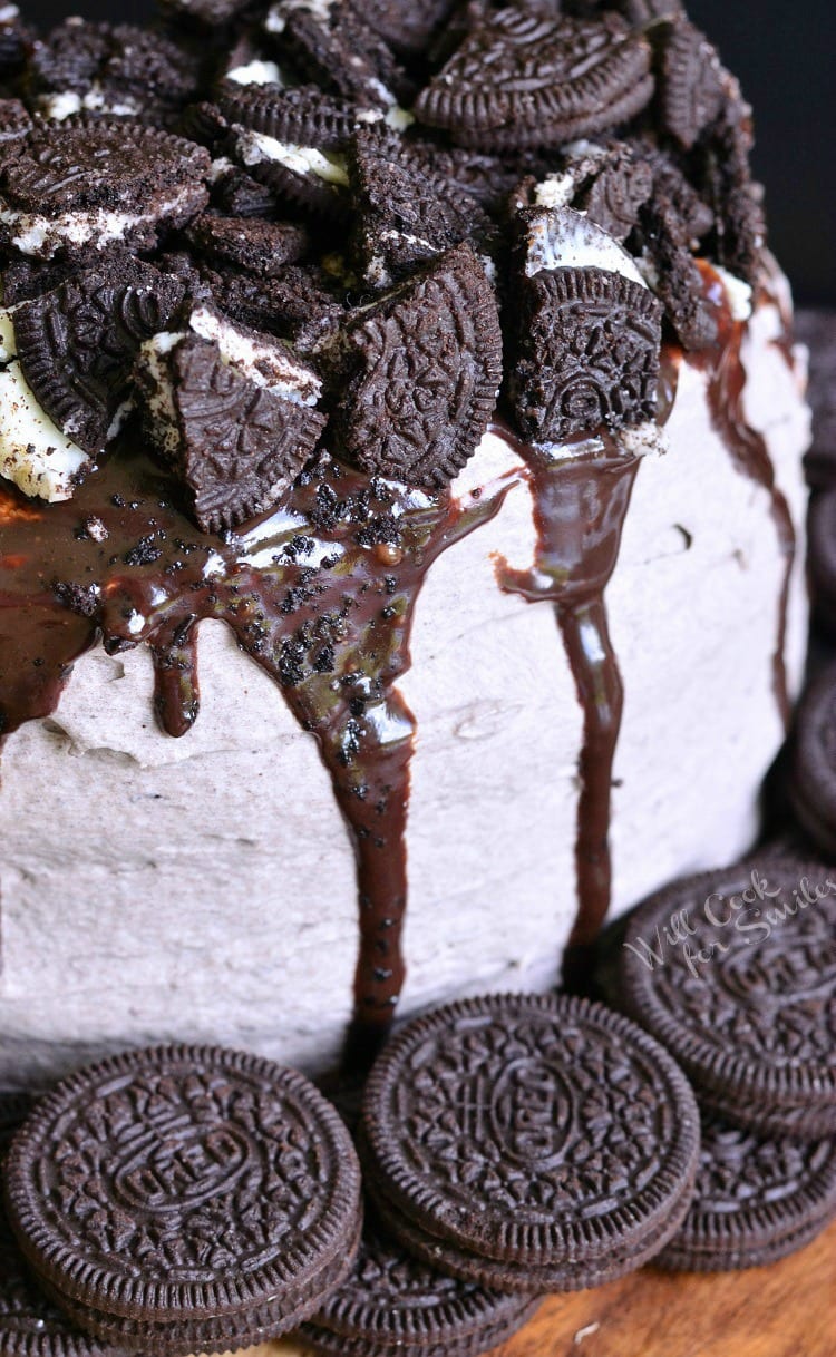 Chocolate Oreo Cake with cut up oreos and chocolate sauce on top of cake and oreos around the bottom on the cutting board 