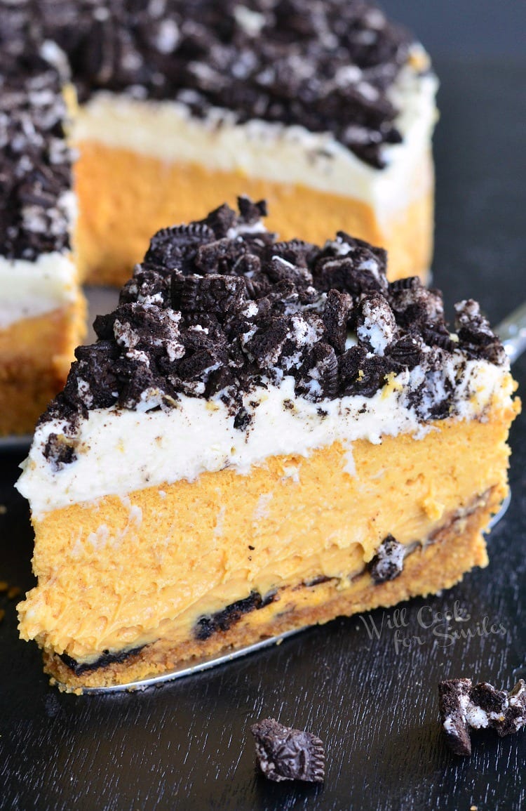 Layered Oreo Pumpkin Cheesecake on a wood table with the rest of the pie in the background 