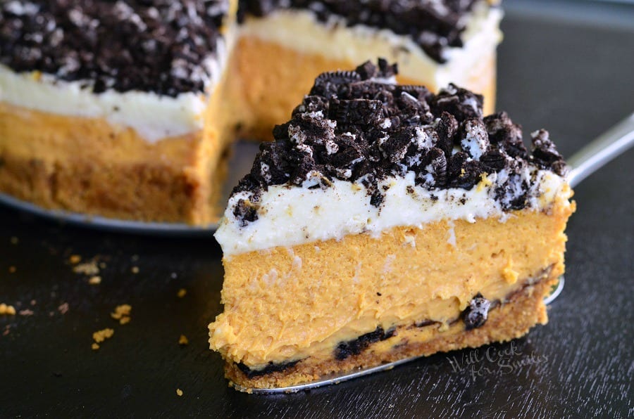 Layered Oreo Pumpkin Cheesecake slice on a pie cutter with the rest of the pie in the background 