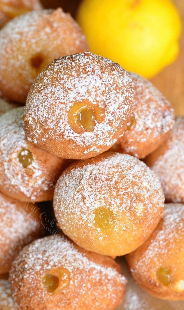 Close up photo of Lemon Curd Filled Doughnut Holes with powdered sugar on top pilled up on a wood plate.