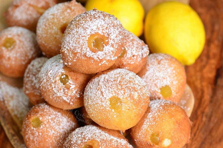 Lemon Curd Filled Doughnut Holes stacked up on plate with powdered sugar on top and lemon in the background 