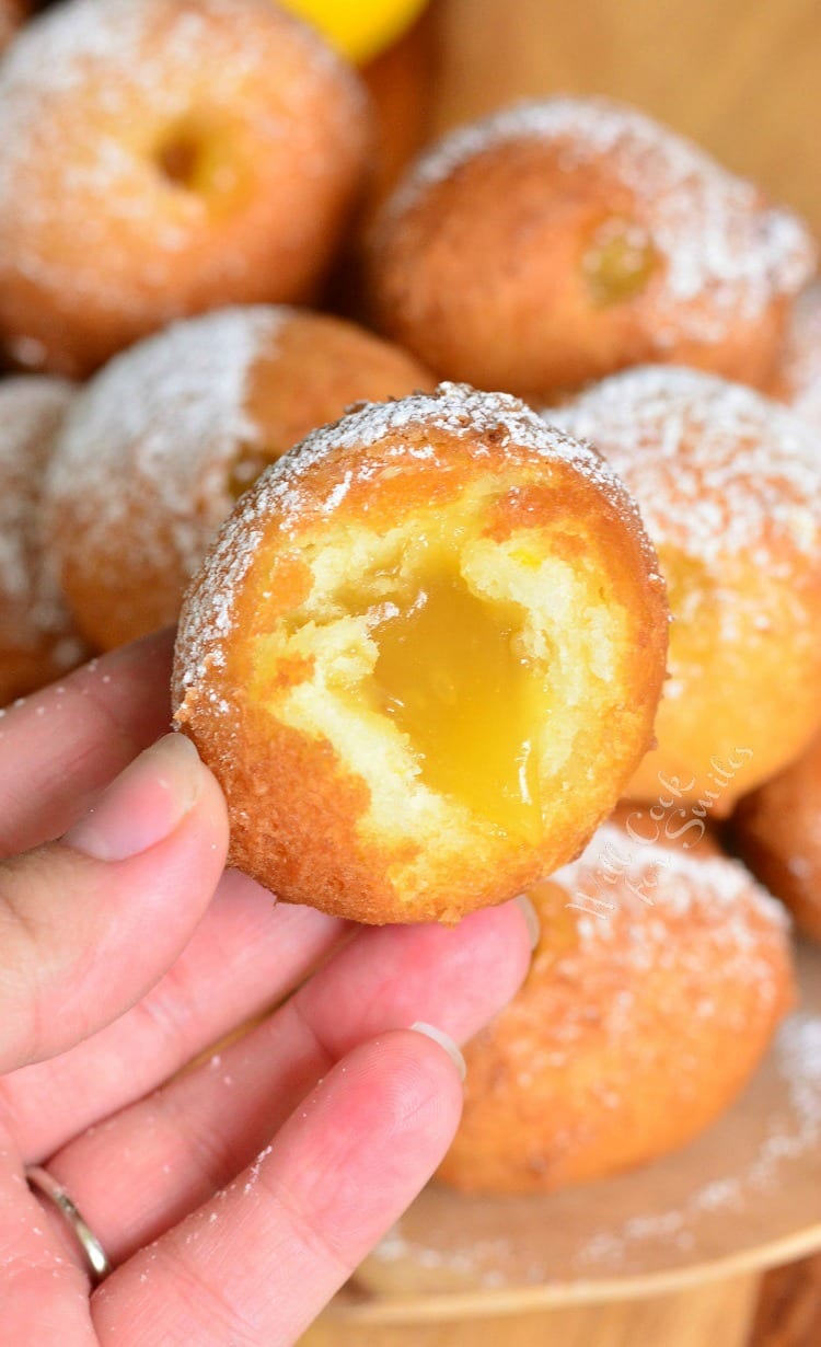 holding Lemon Curd Filled Doughnut with a bite out of it and the rest of the donuts in the background 