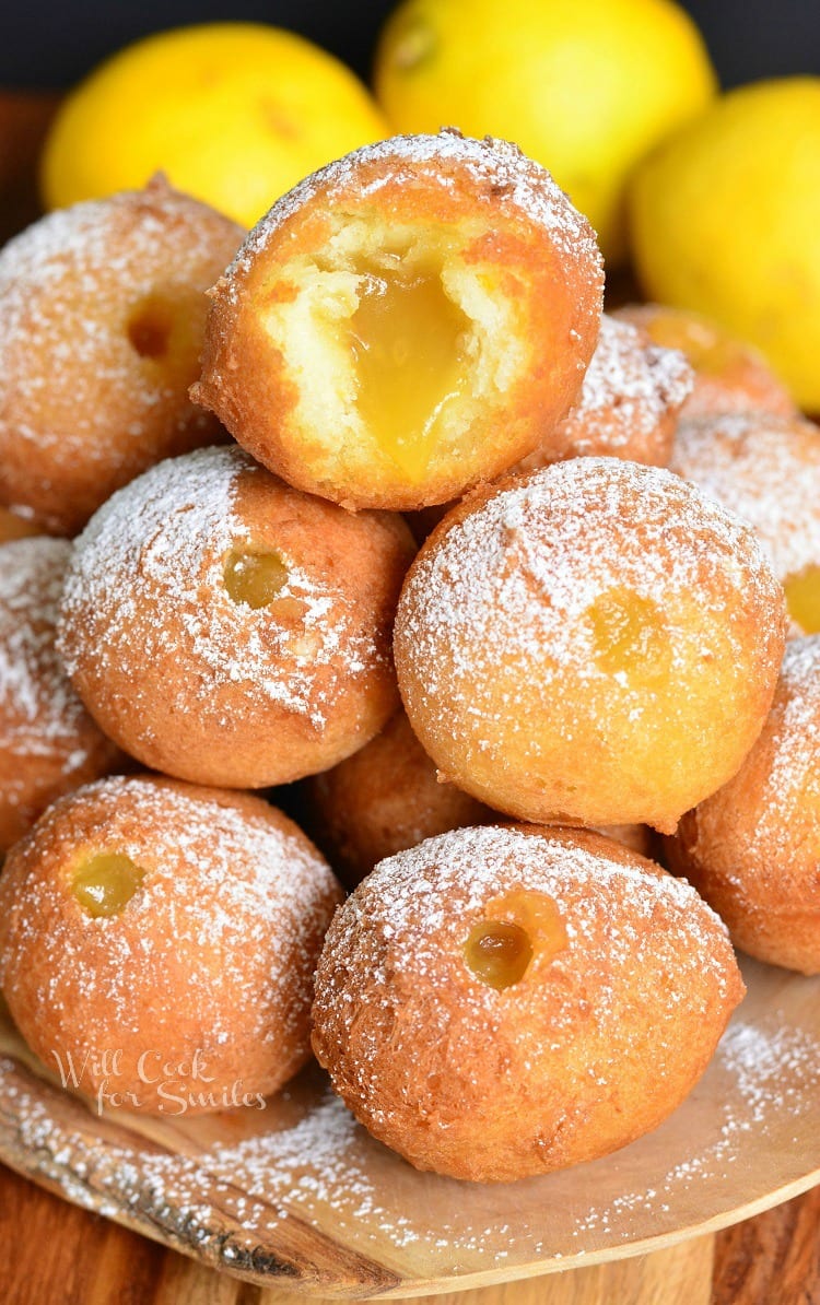 close up of a stack of lemon donut holes with a bite out of the top one to show the lemon curd. 