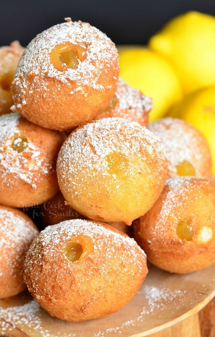 Lemon Curd Filled Doughnut Holes with powdered sugar on top pilled up on a wood plate 