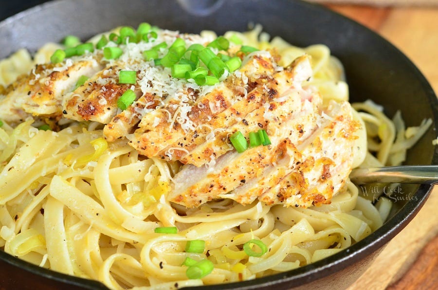 Lemon Pepper Chicken over Fettuccine in a cast iron skillet with green onions on top 