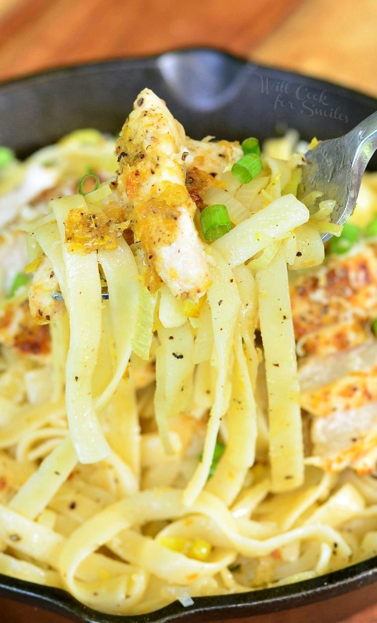 Lemon Pepper Chicken over Fettuccine in a cast iron skillet with green onions on top with a fork 