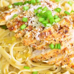 Black skillet filled with lemon pepper chicken fettuccine topped with scallions and parmesan cheese as viewed from above.