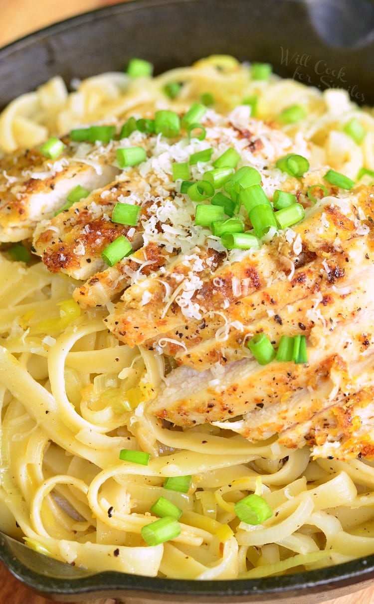 Lemon Pepper Chicken over Fettuccine in a cast iron skillet with green onions on top 