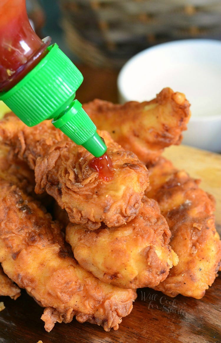 putting Sriracha on fried Chicken Tenders stacked up on a cutting board 