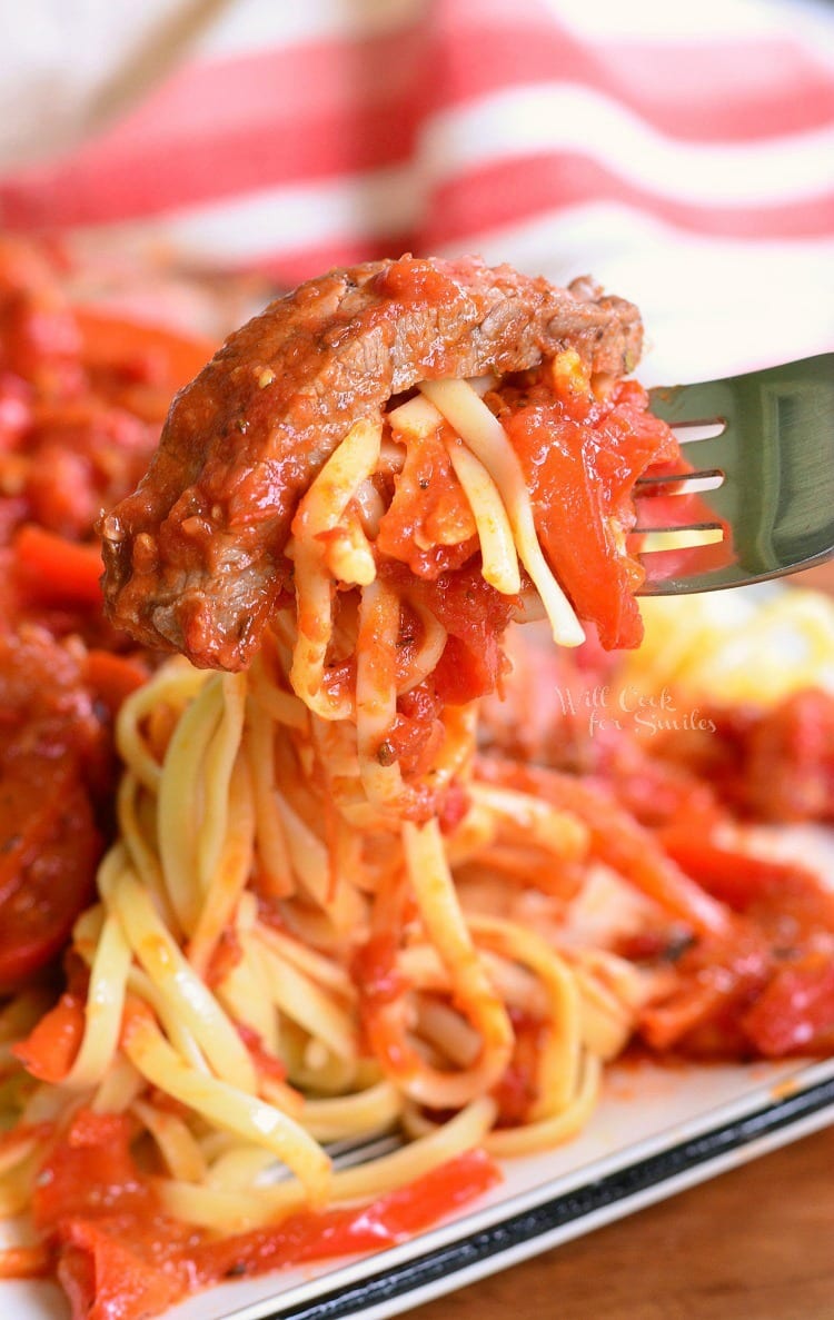 Steak Pizzaiola Linguine being lifted off white plate with a fork 