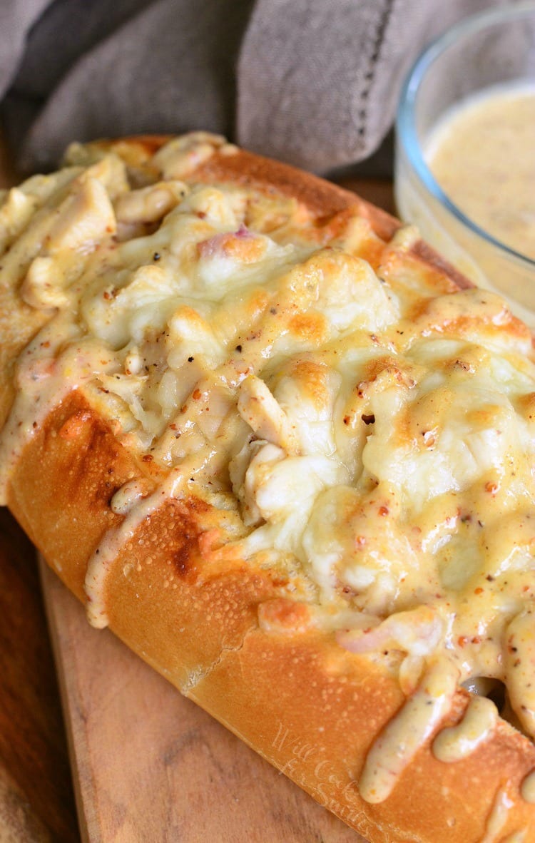 top view Chicken Sub with white bbq on top on a cutting board with a bowl of white bbq sauce in the background to the right