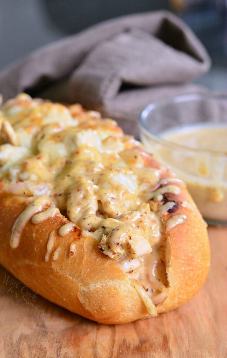 White BBQ chicken sub on a wooden table with a small glass dish holding white BBQ sauce in the background as viewed close up