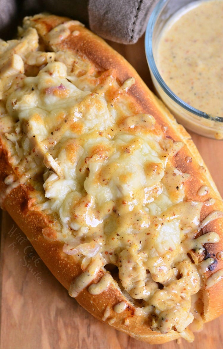 top view Chicken Sub with white bbq on top on a cutting board with a bowl of white bbq sauce in the background to the right