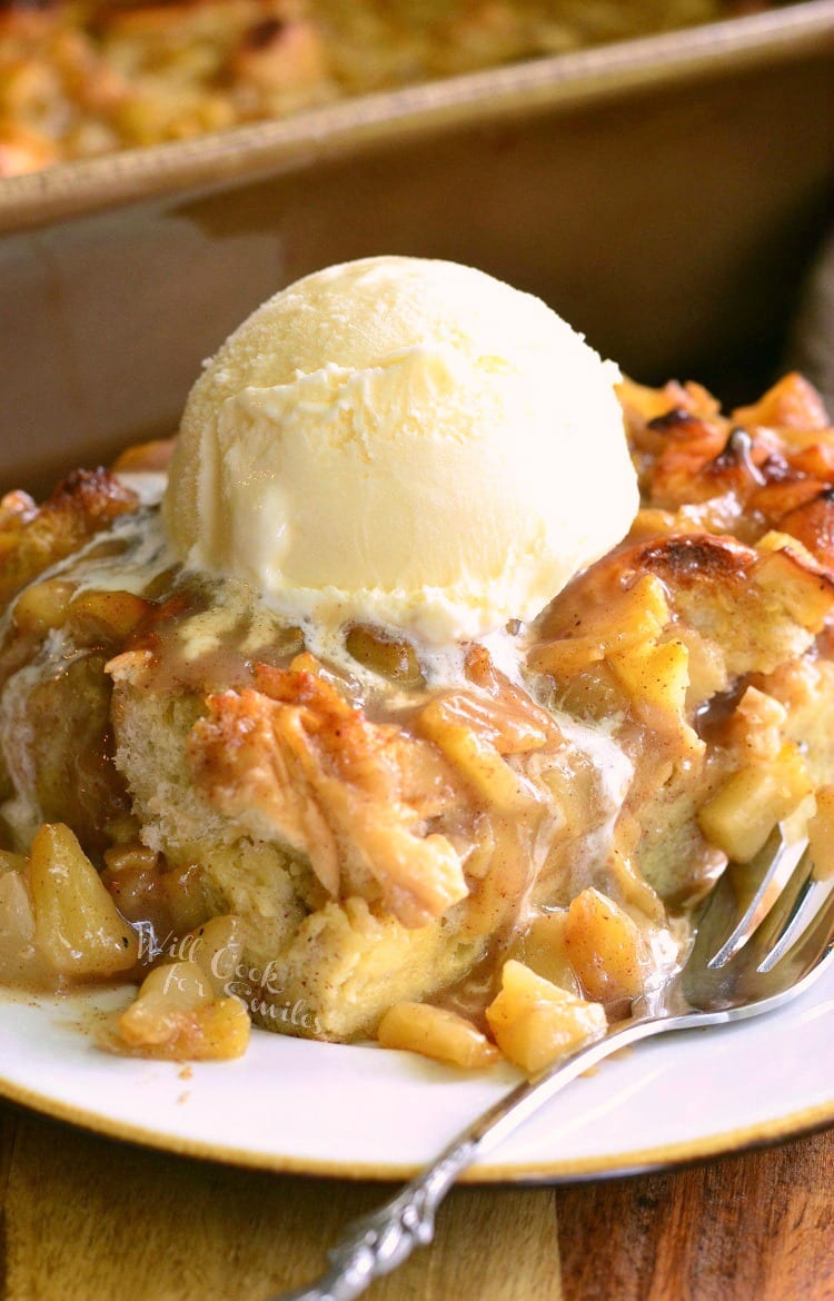 Apple Pie Bread Pudding with ice cream on top on a white plate with a fork to the right 