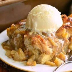 round decorative bowl filled with apple pie bread pudding topped with ice cream and a fork leaning on the side of the bowl viewed close up.