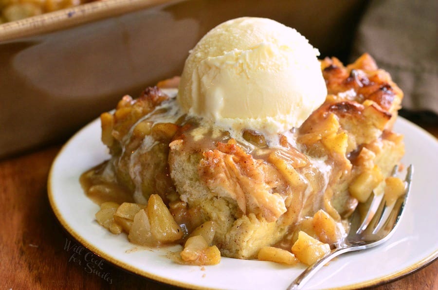 Apple Pie Bread Pudding on a white plate with a scoop of vanilla ice cream on top with a fork to the right 