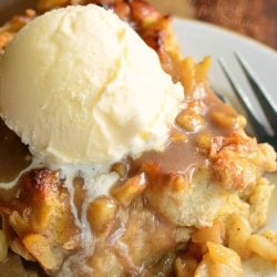 round decorative bowl filled with apple pie bread pudding topped with ice cream and a fork leaning on the side of the bowl.