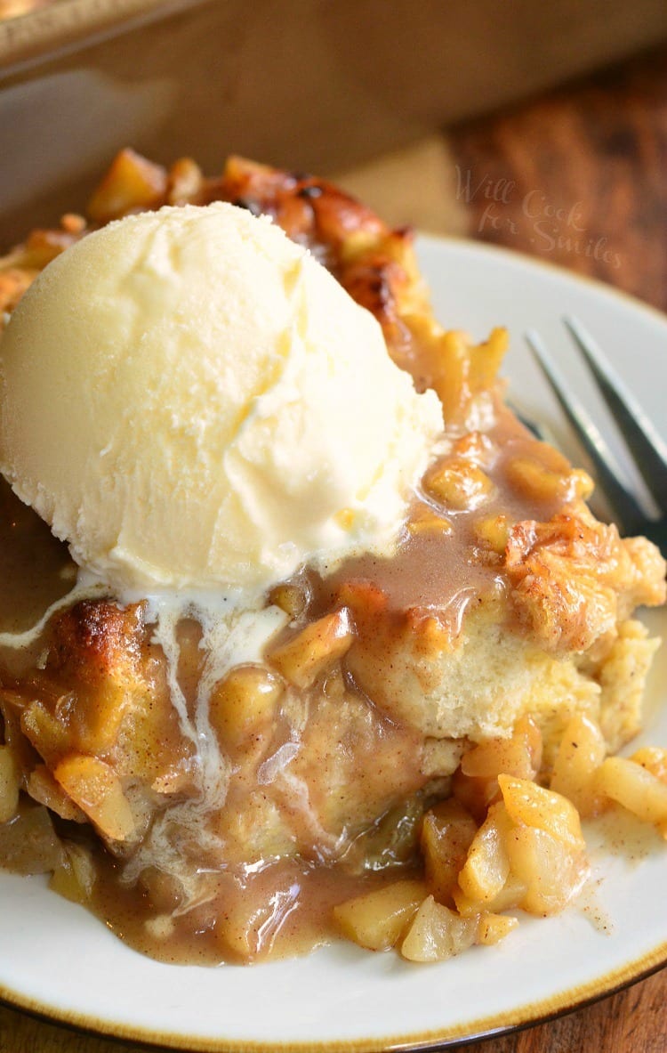 Apple Pie Bread Pudding with a scoop of vanilla ice cream on top on a white plate with a fork to the right 