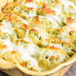 Cream colored baking pan with cheesy pesto chicken stuffed shells as viewd from slightly above and close up.