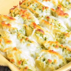 Cream colored baking pan with cheesy pesto chicken stuffed shells as viewd from slightly above.