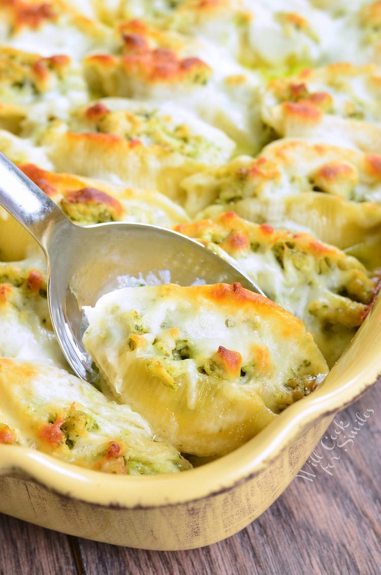  Cheesy scooping with a spoon some Pesto Chicken Stuffed Shells with cheese melted on top in a yellow baking dish 