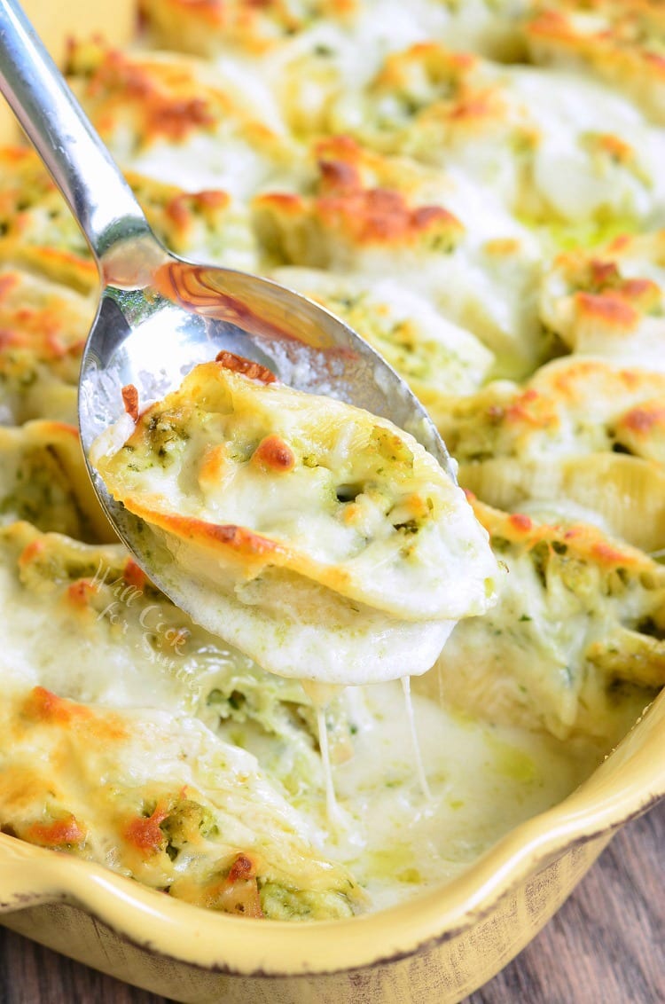  Cheesy scooping Pesto Chicken Stuffed Shells with cheese melted on top out of a yellow baking dish with a metal serving spoon 