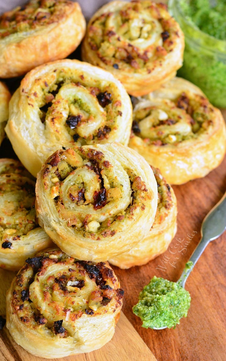 Pesto Chicken and Sun Dried Tomato Pinwheels on a cutting board with a spoon of pesto to the left 