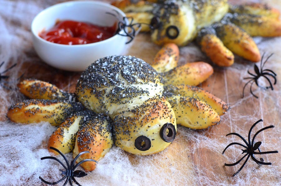 Pretzel Spiders on cutting board with fake spider web, red dipping sauce in a white bowl and fake spiders around it 