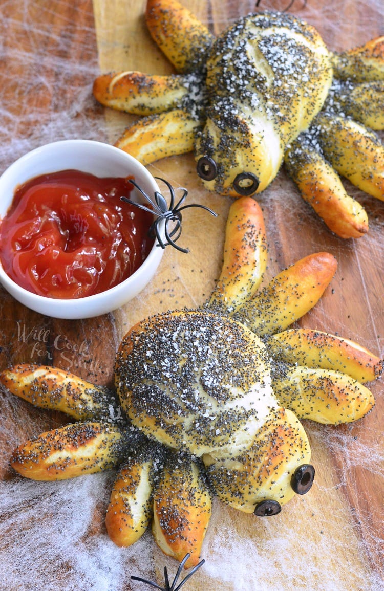 top view Pretzel Spiders with olive eyes and dipping sauce in a white bowl with fake spiders 