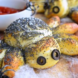 Decorative pretzel spiders on faux web and a wooden table with plastic spider rings around them.