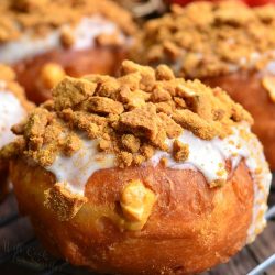 cheesecake pumpkin doughnuts with gingersnap crumb topping on a wire rack resting on a wooden table as viewed close up.