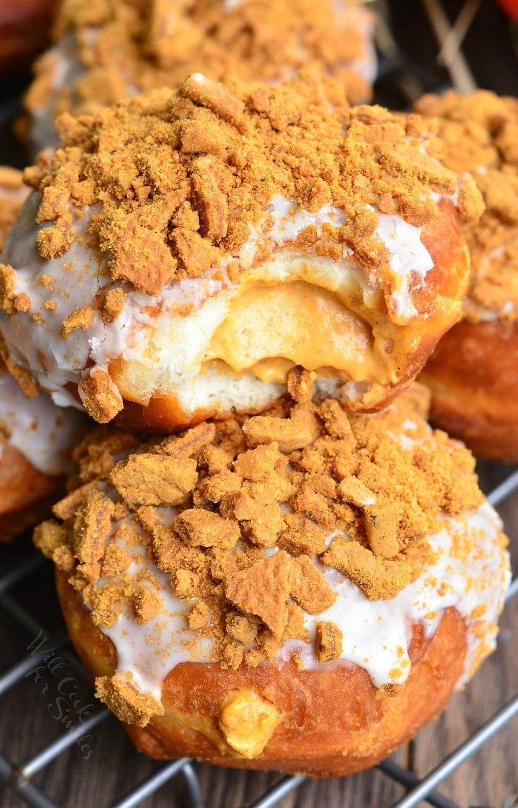 Pumpkin Cheesecake Doughnuts with Gingersnap Crumb on top with a bite taken out of one on a cooling rack 