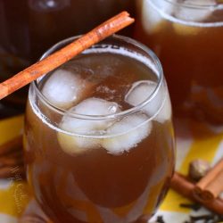 Glass filled with spiced iced tea with an additional glass and a pitcher filled with spiked tea in the background