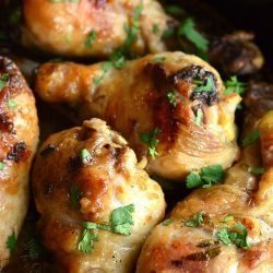 large black skillet with coconut lime chicken drumsticks on a wooden table with limes in the background