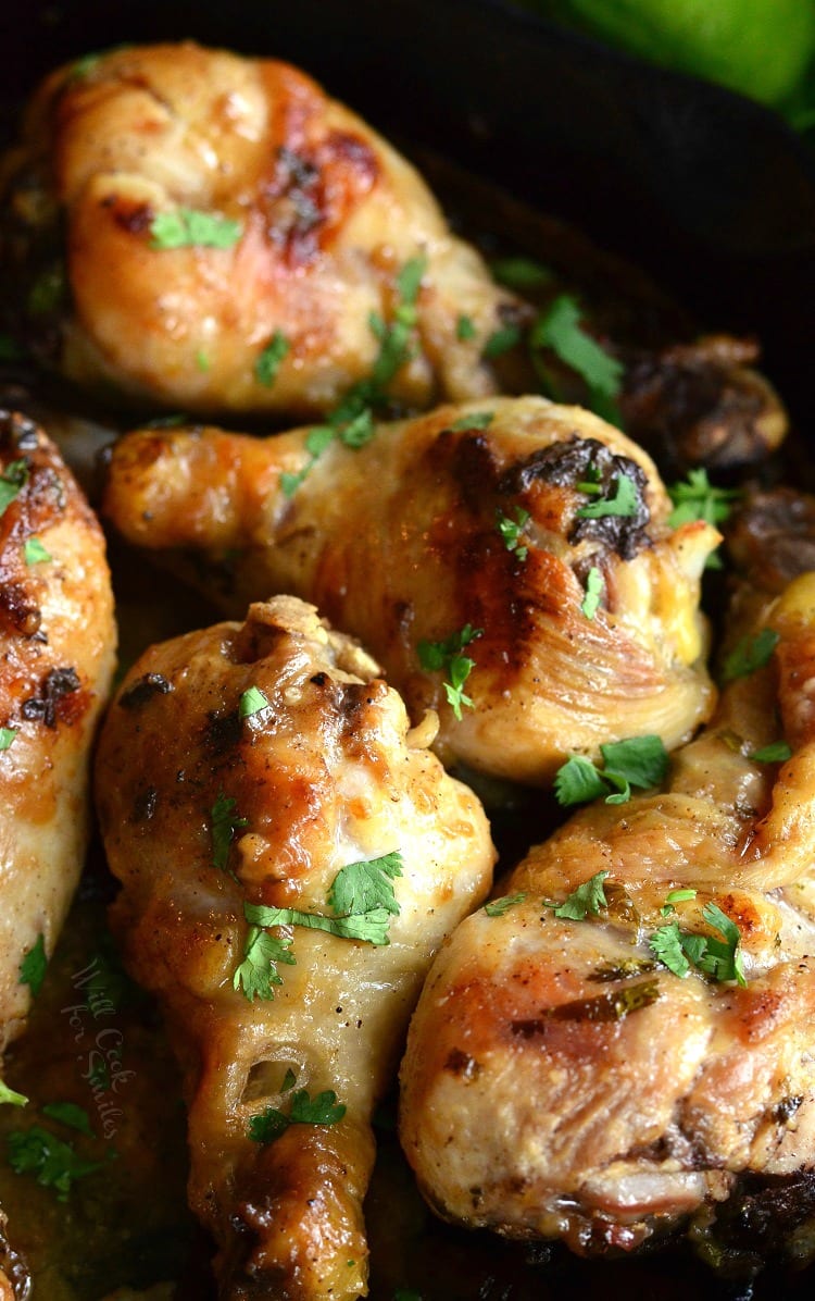 large black skillet with coconut lime chicken drumsticks on a wooden table with limes in the background