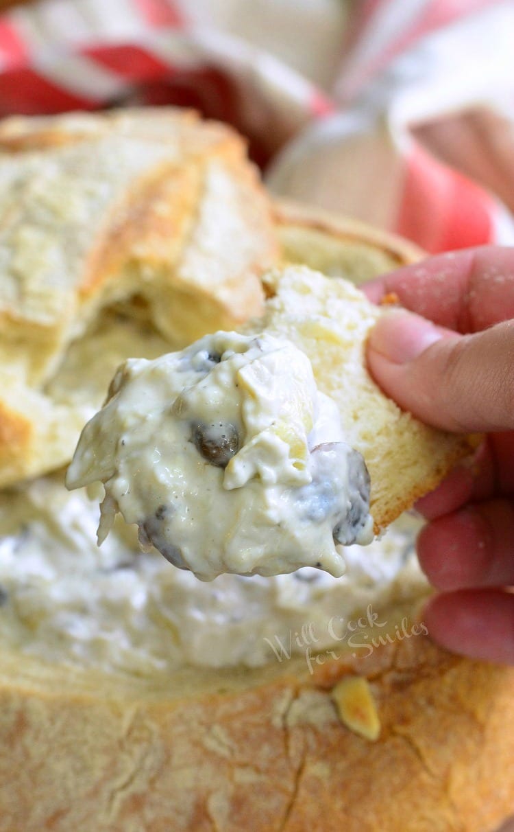 dipping a piece of bread into Fontina Mushroom Artichoke Dip.