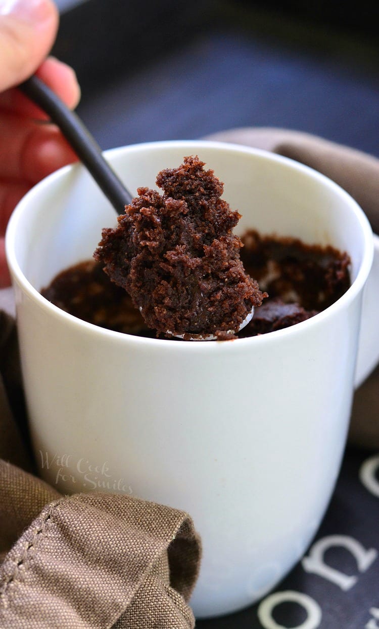 Chocolate cake in a white coffee mug with a spoon lifting some out 