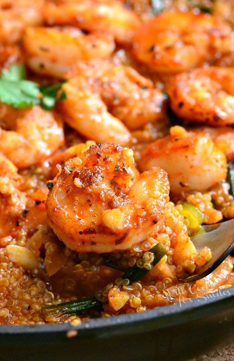 skillet filled with cajun shrimp and quinoa with a spoon lifting one shrimp from the dish.