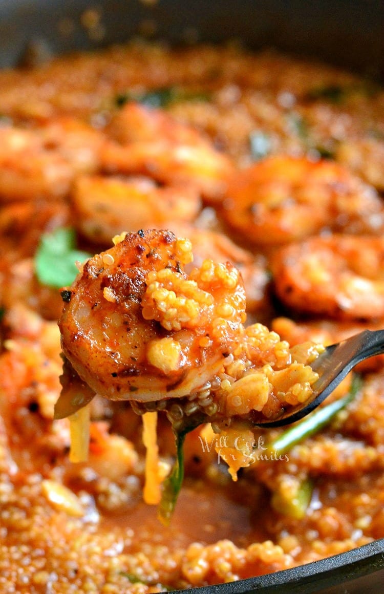 Shrimp and Quinoa on a fork with a cast iron skillet of shrimp and Quinoa in the background 