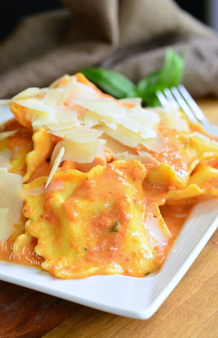 Ravioli in a creamy red bell pepper and basil sauce topped with shaved Parmesan cheese on a white plate 