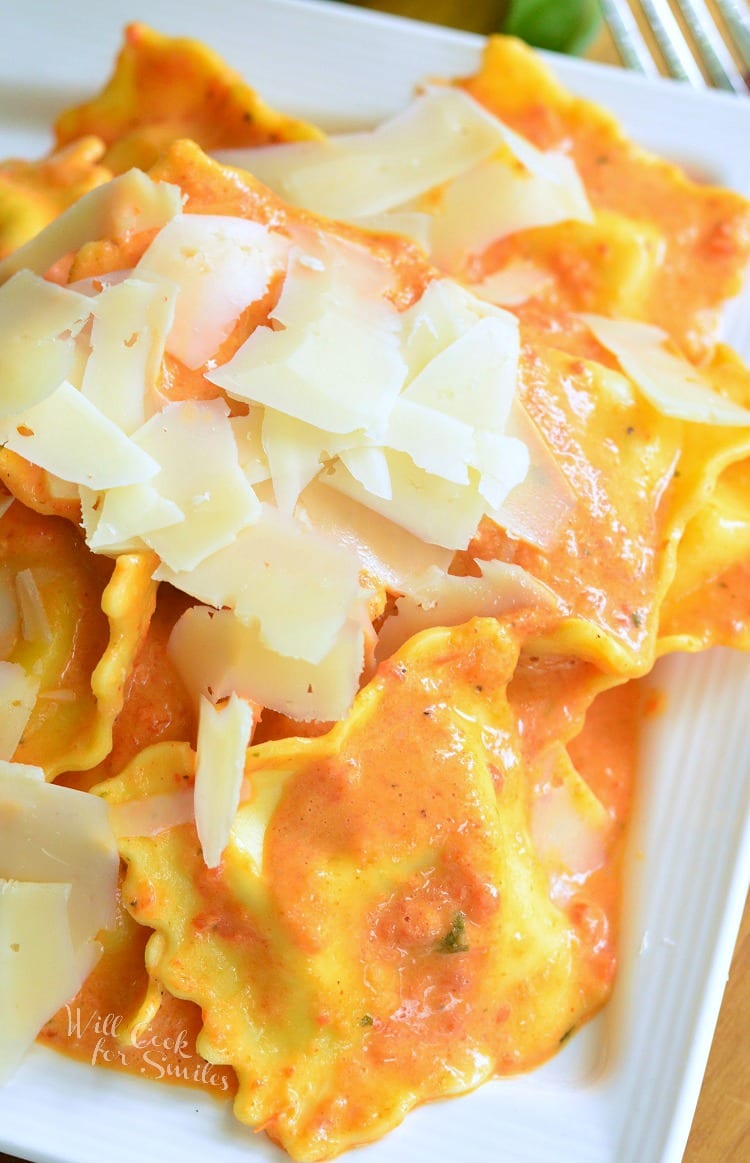 top view of Ravioli in a creamy red bell pepper and basil sauce topped with shaved Parmesan cheese on a white plate 