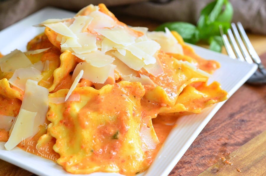 Ravioli in a creamy red bell pepper and basil sauce topped with shaved Parmesan cheese on a white plate 