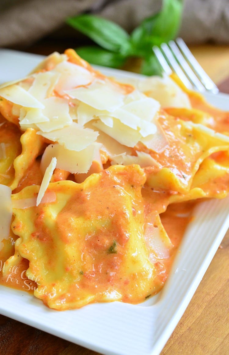 Ravioli in a creamy red bell pepper and basil sauce topped with shaved Parmesan cheese on a white plate 