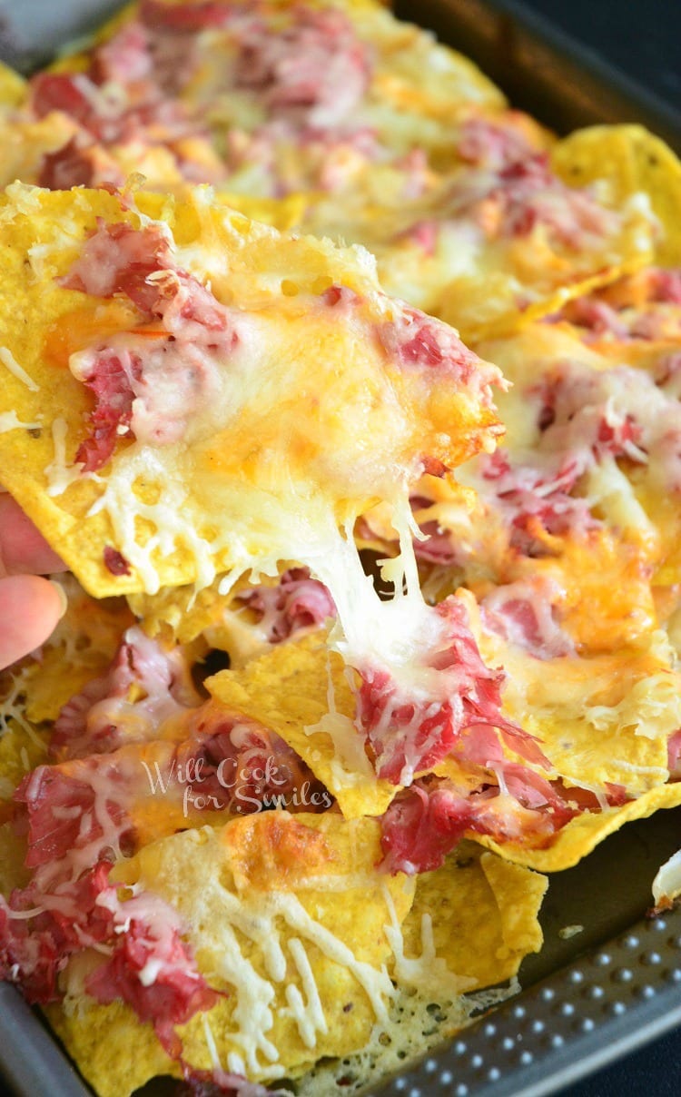 lifting a Tortilla chips, corn beef, and cheese of of a baking sheet 