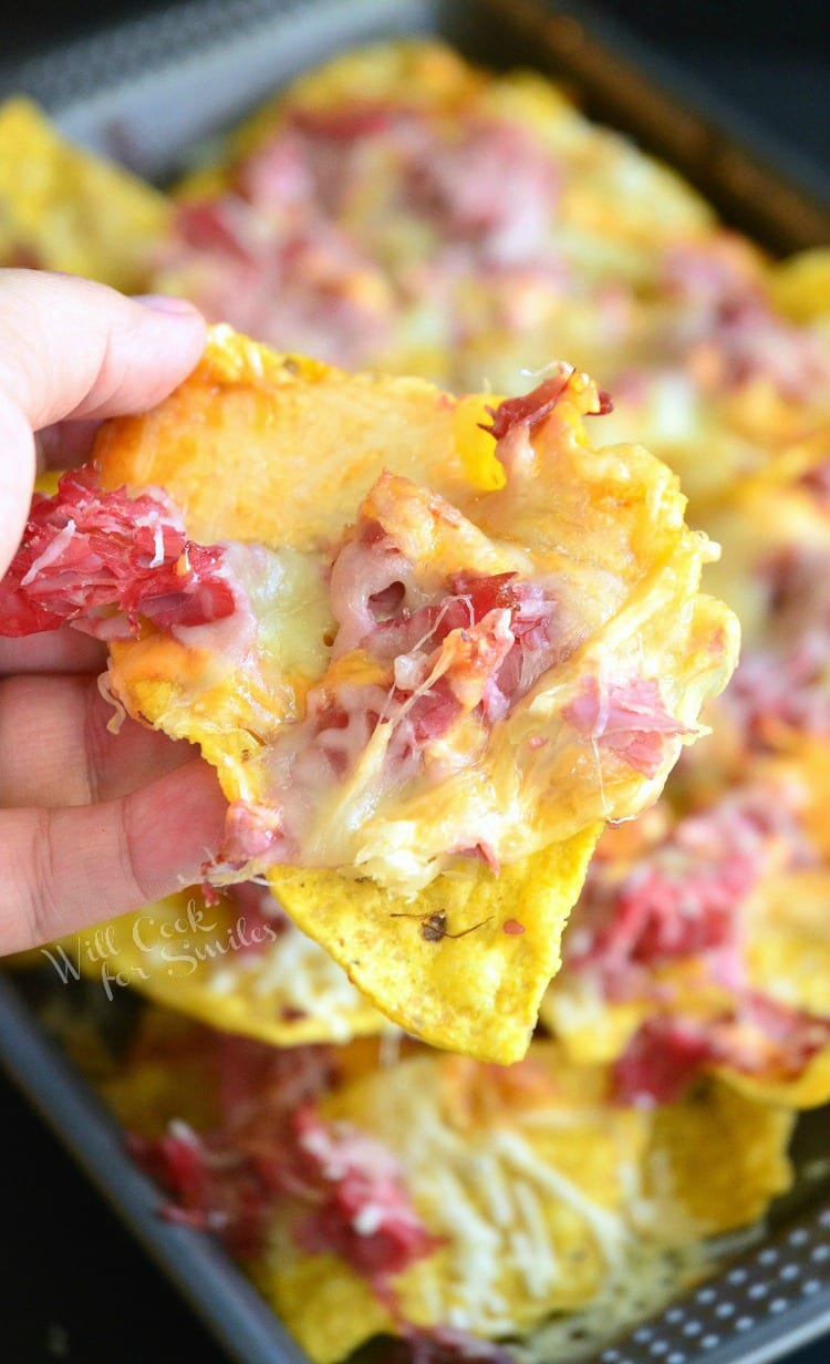 lifting Tortilla chips, corn beef, and cheese off of a baking sheet 